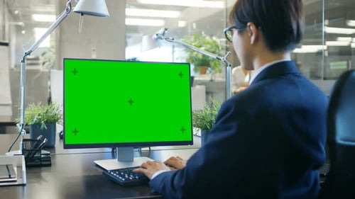 In the Office Businessman works at His Desk on a Personal Computer with Mock-up Green Screen. Colle