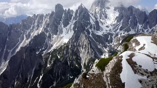 Uma cordilheira rochosa afiada que se eleva acima de um incrível vale verde com neve. Dia ensolarado com nuvens a