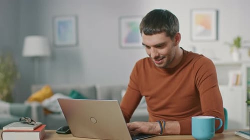 Young Man Uses Laptop at Desk, Celebrates Success