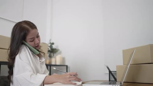 Woman Talking on Cellphone While Writing in Notebook