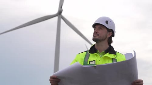 Wind turbine technician in safety gear with laptop and radio at renewable energy farm