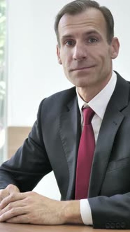 Man in Suit Sits at Desk Smiling
