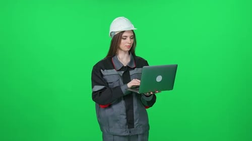 Young Woman Worker in a Uniform and Protective Helmet Technical Engineer Stands and Uses a Laptop on