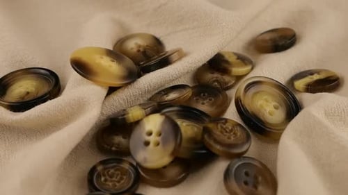 Natural bone color buttons fall on beige natural linen fabric. Slow motion.