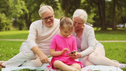 Grandparents and Granddaughter Using Mobile Phone in Park