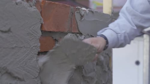 Close up view of a construction technician applying cement mix with trowel at side wall in backyard.