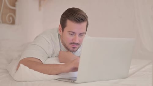 Jeune homme levant le pouce tout en utilisant un ordinateur portable couché sur le ventre