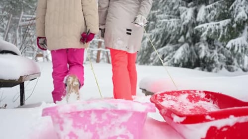 Two Girls Walking with Sleds in Snowy Playground