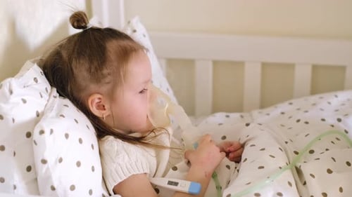 A mother measures the body temperature of a sick child who inhales while lying in bed