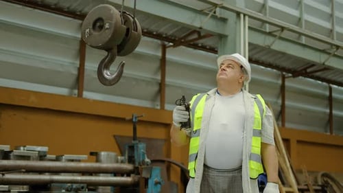 Un ingénieur mature portant un casque de sécurité et un gilet de sécurité utilise une télécommande pour contrôler une grue robuste