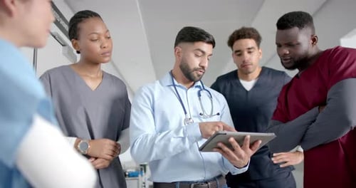 Diverse male and female doctors discussing work using tablet in hospital corridor, slow motion
