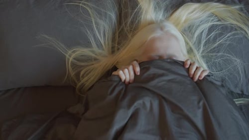 Blonde Woman Lying in Bed Pulls Blanket Over Face