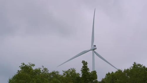 Renewable Energy Wind Turbine Spinning Generating Clean Electricity with Trees Below and Clouds 4K