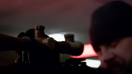 Serious professional killer holding sniper rifle looks through scope outdoors