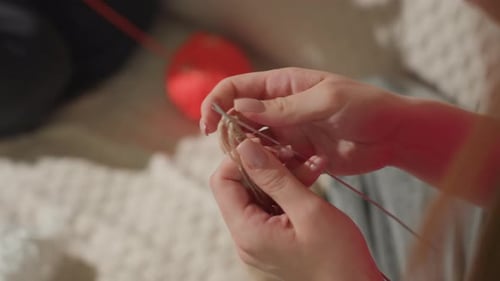 Closeup of Hands Creating Stitches with Red Yarn in Cozy Setting Detailed View of Fingers Working on