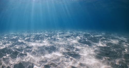 Océano azul transparente con rayos de sol, fondo arenoso y olas bajo el agua