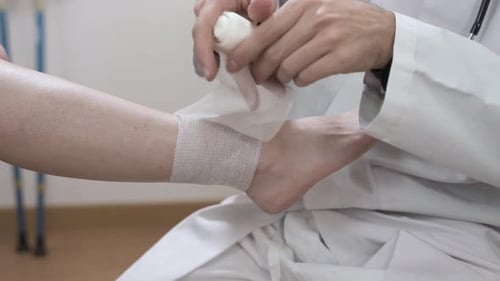 Doctor Wrapping Patient Ankle with White Bandage