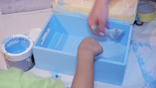 Child and Adult Painting a Blue Wooden Box