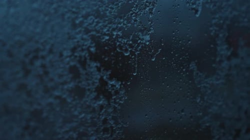 4K Close-Up of Snow and Raindrops Dripping Down a Window in Slow Motion
