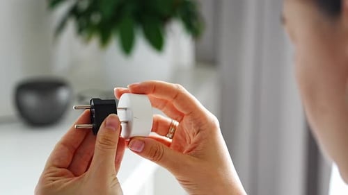 Frau vergleicht elektrische Steckeradapter für verschiedene Steckdosen zu Hause, auf internationalen Reisen und