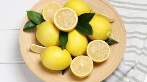 Ripe lemons and leaves spinning on white wooden table, top view