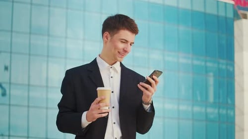 Young Adult in Suit Using Phone With Coffee