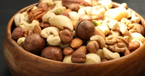 Woman putting different nuts into bowl at table, closeup