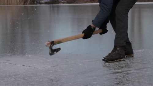 Person, die im Winter das Eis eines gefrorenen Sees bricht.