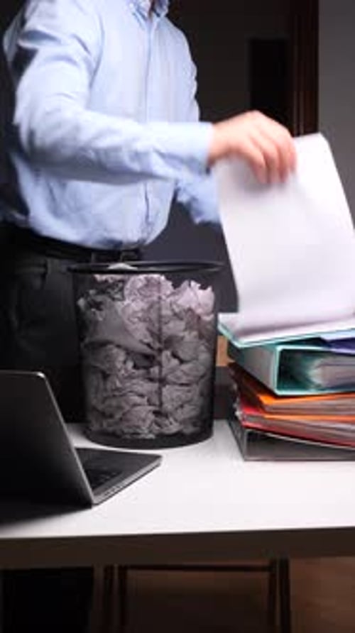Man crumples paper at desk and throws in trash