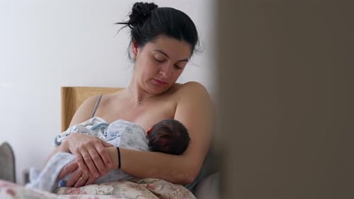 Mother Nursing Newborn Baby in Bed at Home