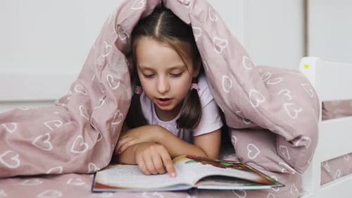 Girl Reads Book in Bed Under Blanket