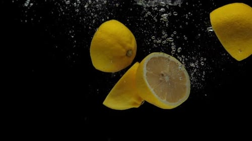 Lemons Dropping into Water with Bubbles on Black