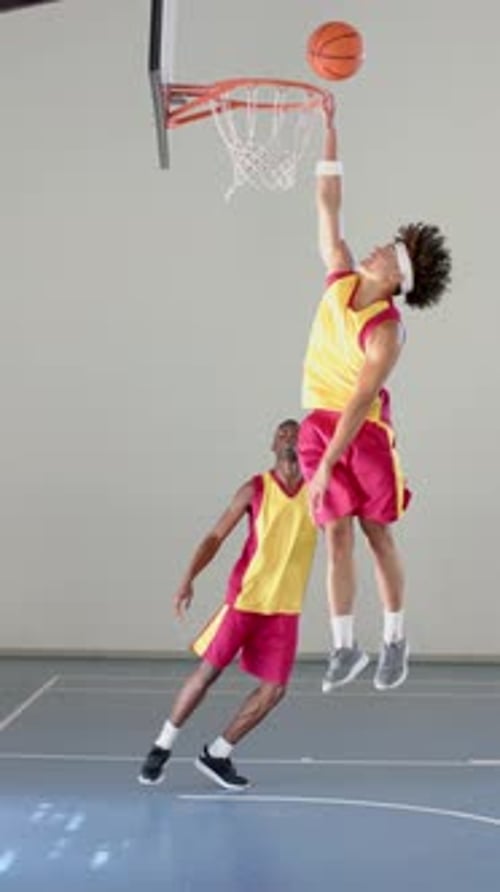 Vertical video: Playing basketball, two men in sports uniforms dribbling on indoor court