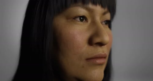 Une femme aux longs cheveux noirs regarde pensivement vers le côté