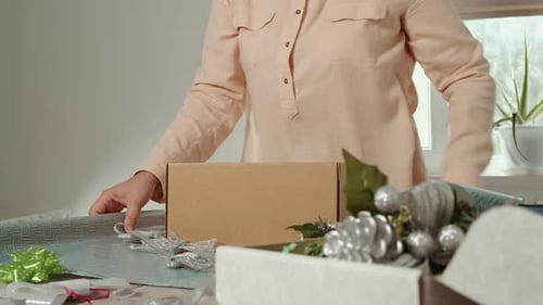 Woman Arranging Christmas Ornaments and Wrapping Supplies on Table