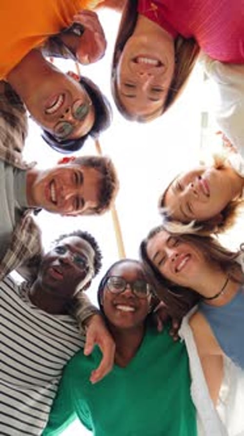 Vista vertical de ángulo bajo de un grupo de amigos multirraciales de pie en un círculo sonriendo y abrazándose