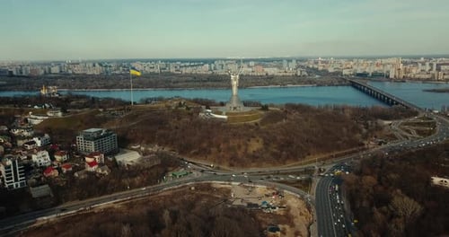 Mutterlandstatue in Kiew mit Fluss Dnipro, ukrainischer Flagge und Skyline der Stadt im Hintergrund