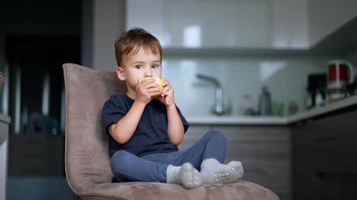 Child Sits and Eats a Yellow Apple