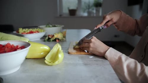 Woman cutting yellow pepper on wooden cutting board
