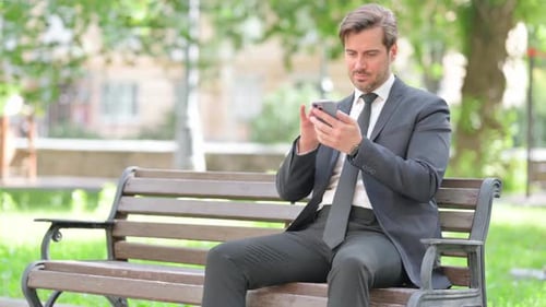 Man in Suit Uses Smartphone on Park Bench
