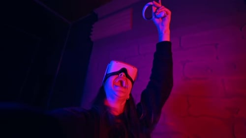 A young interested woman playing in VR games using VR glasses and controllers, filming herself on ca