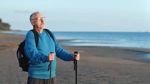 Relaxed Grandfather Scandinavian Walking Stick and Backpack Enjoy Sunset Natural Light at Sea Beach