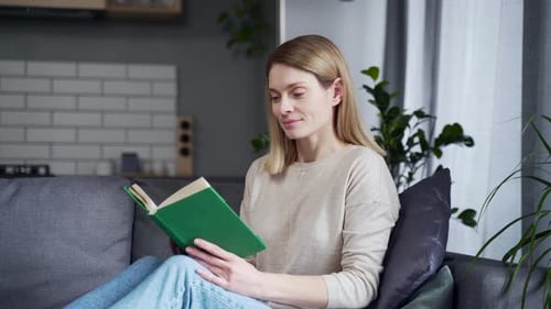 Close-up. Mature beautiful woman reading a book while sitting on the sofa in the living room at home