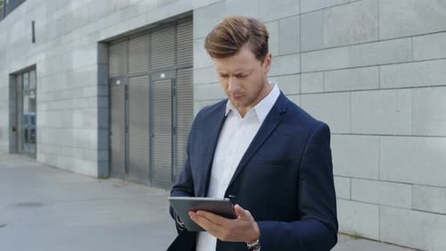 Serious businessman browsing internet on digital tablet in modern city street