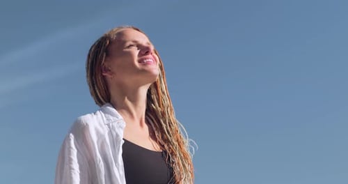 Mulher feliz e relaxada respirando ar fresco, levantando os braços sobre o céu azul no verão, sonhando com liberdade e