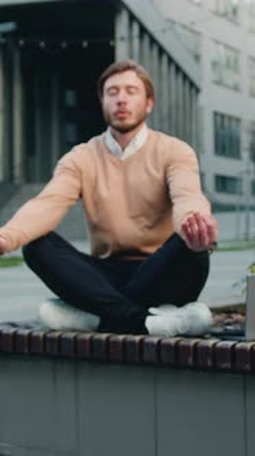 Handsome Caucasian Bearded Man in Glasses Relaxing Sitting in the Lotus Position on the Bench of the