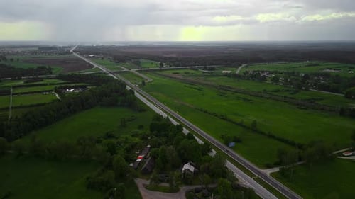Aerial View of Rural Landscape with Road Winding Through Green Fields Under Cloudy Sky Showcasing