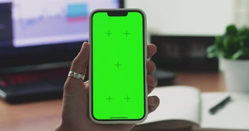 A Woman's Hand Phone with Green Mockup Screen Chroma Key Holds a Smartphone of the Workspace