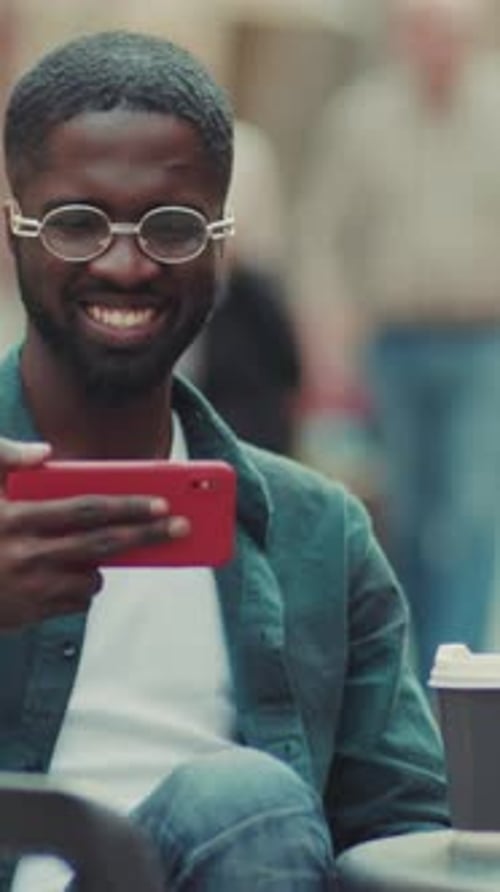 Young Man Actively Engaging with His Smartphone in a Casual Social Setting Outdoors