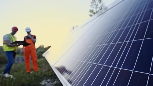 Male Workers Standing in Uniform and Helmets Near Solar Panels Outdoors in Soft Focus